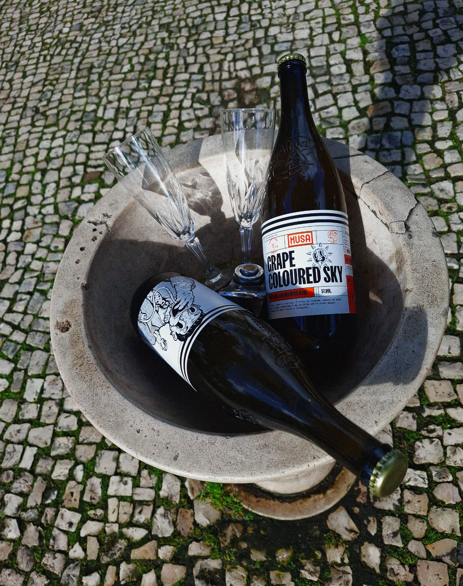 Imagem de uma garrafa de Grape Colored Sky - Grape Ale, colaboração Cerveja MUSA, Fermentage e Nat’Cool, a ser segurada numa mão com uma flute de champanhe, e o céu atrás